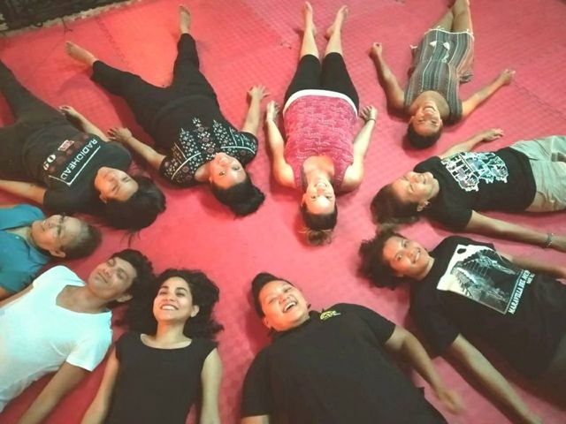 Un cercle de participants allongés au sol, souriants, pendant une séance de travail somatique et vocal